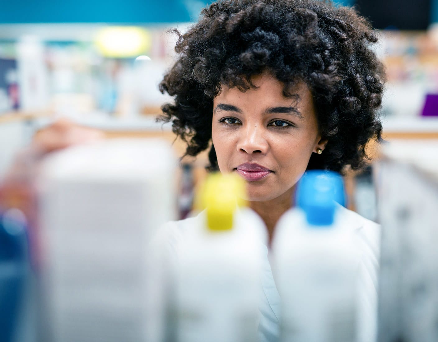 A woman with curly hair examines a bottle of shampoo, contemplating its features and benefits.